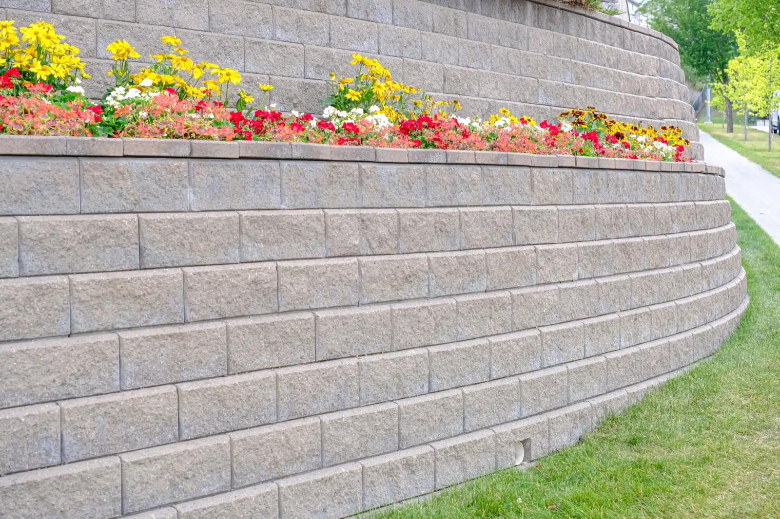 Grey split-face block retaining wall in running bond with a drain outlet at the base