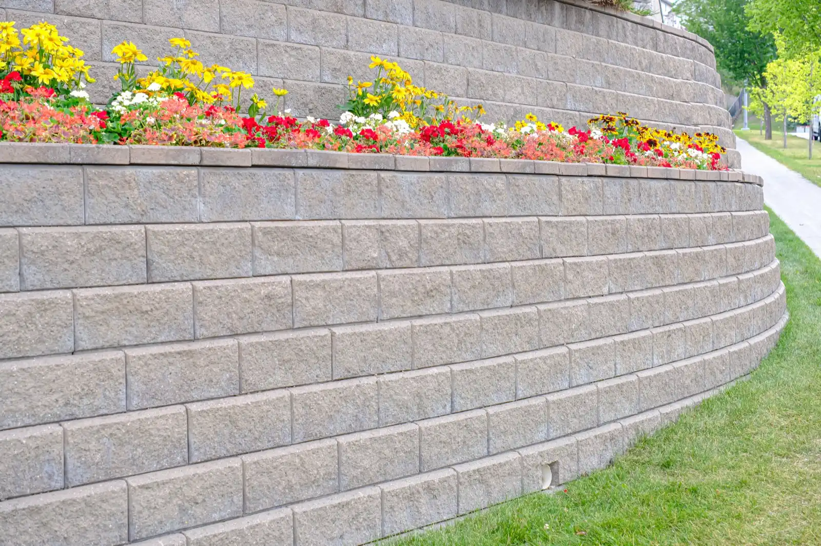 Grey split-face block retaining wall in running bond with a drain outlet at the base