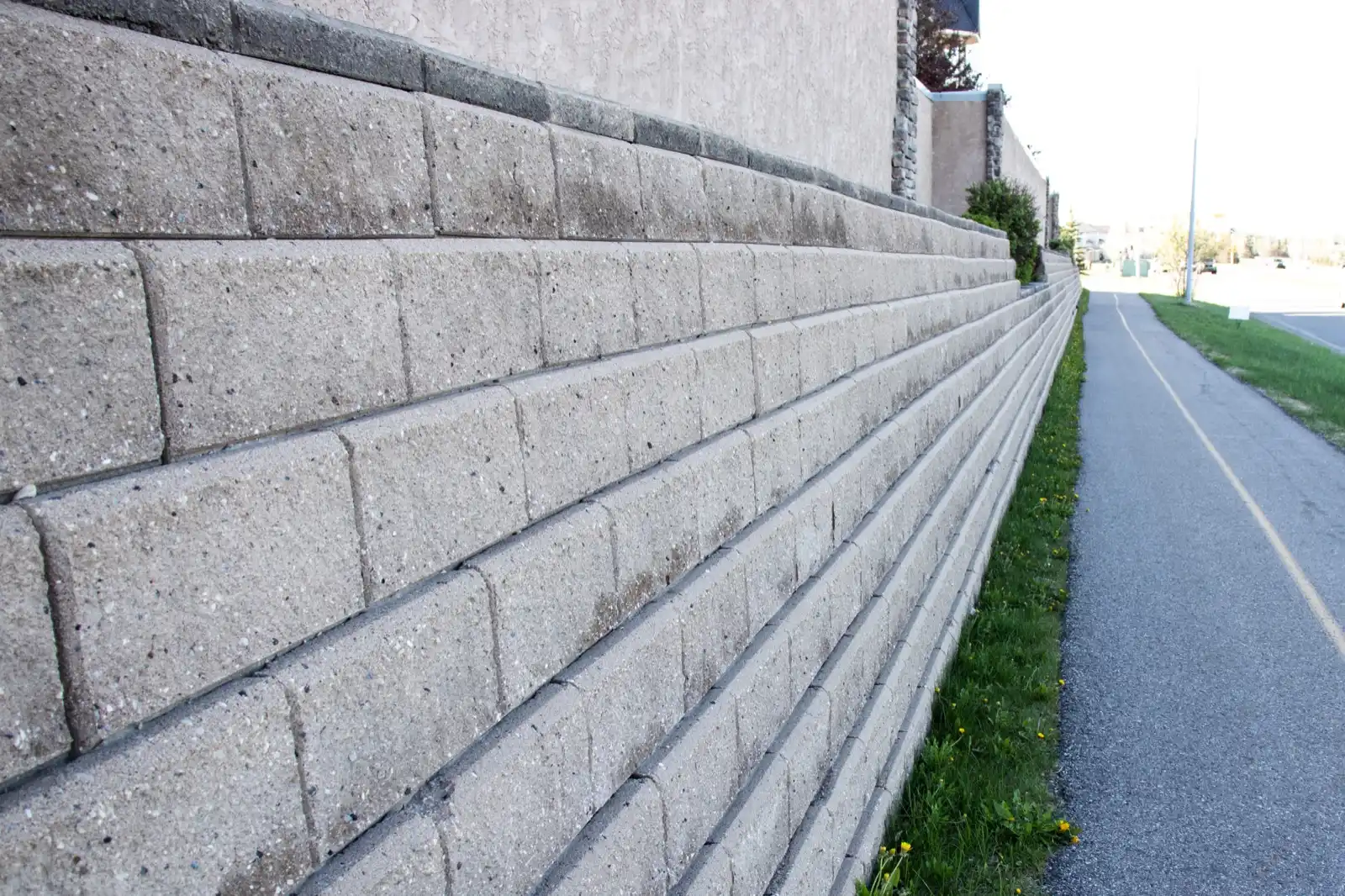 Tall segmental block retaining wall stepping back course by course beside a path