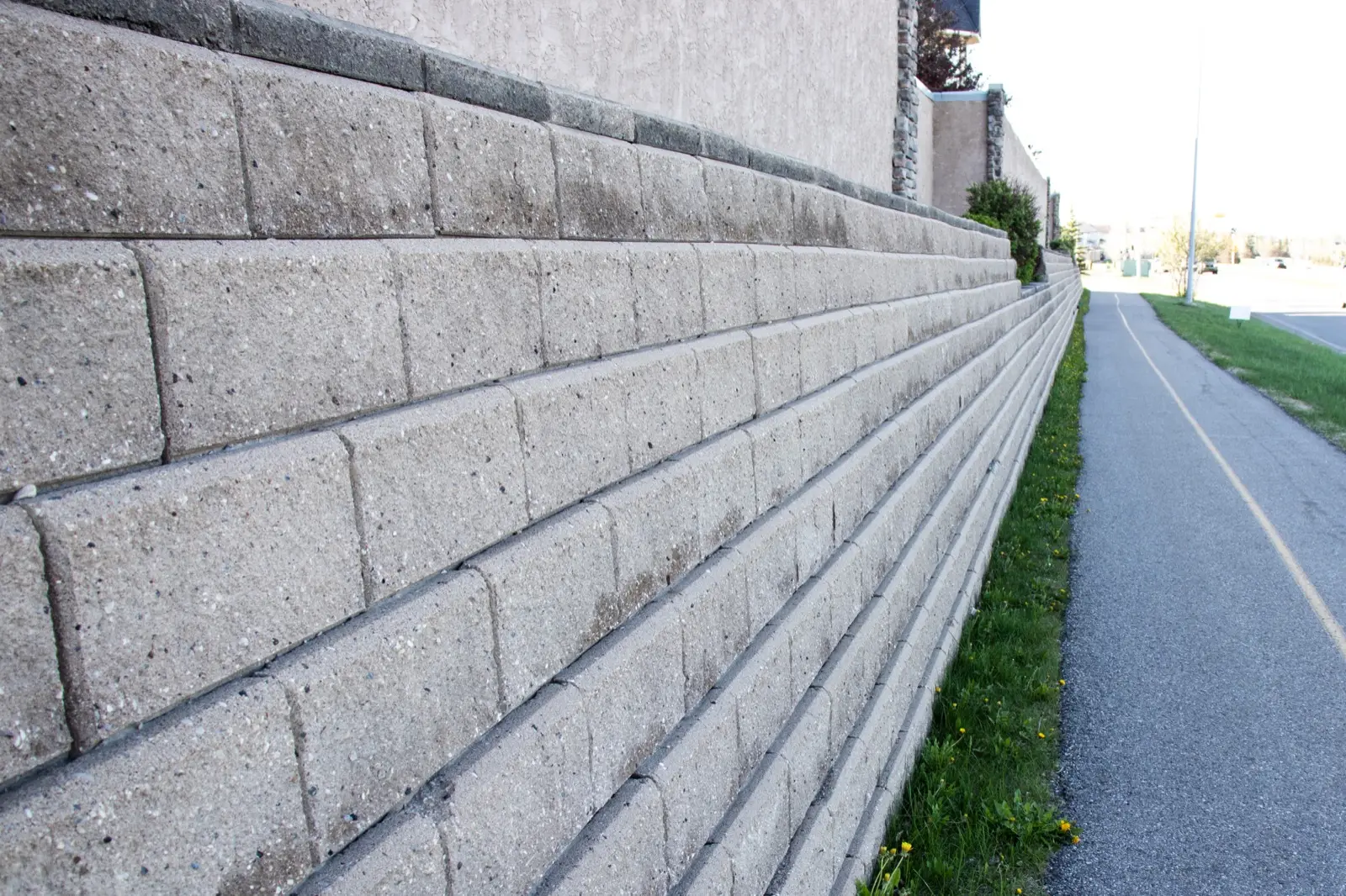 Tall segmental block retaining wall stepping back course by course beside a path