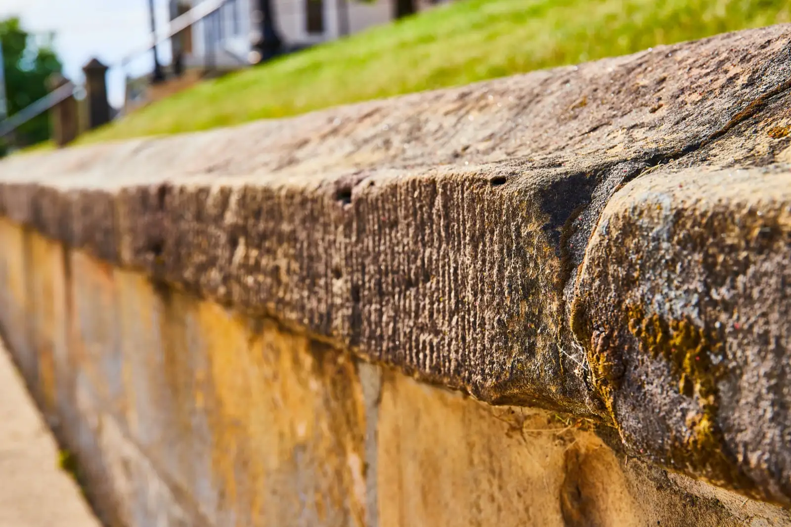 Weathered retaining wall cap with moss and staining below a lawn slope